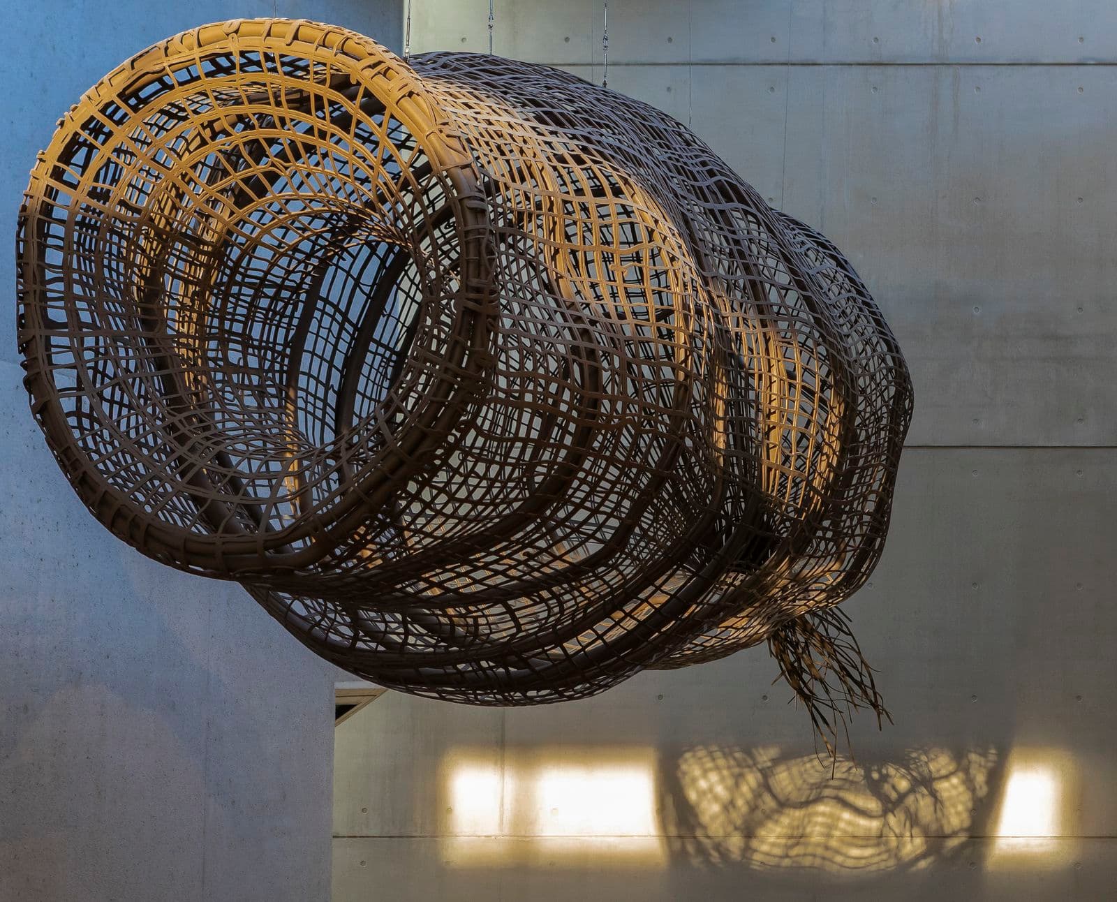 A large metal sculpture of an Indigenous Australian fish trap is hanging from the ceiling in a large gallery foyer