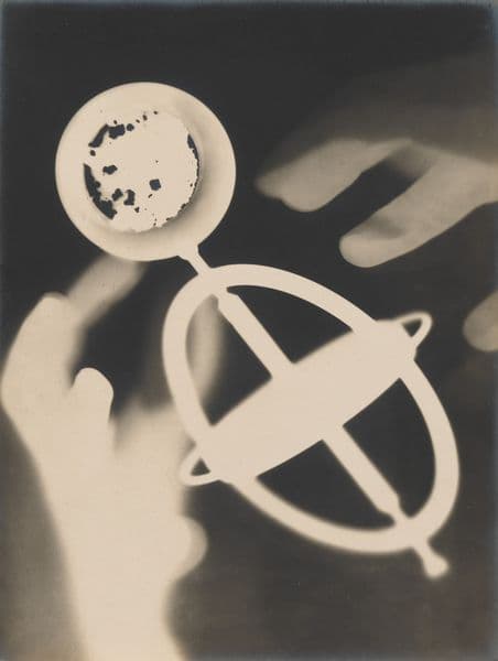 A sepia toned photogram showing a pair of hands around a compass-like shadow.