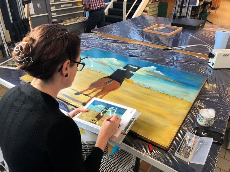 Photograph of Sidney Nolan's Ned Kelly being observed by painting conservator