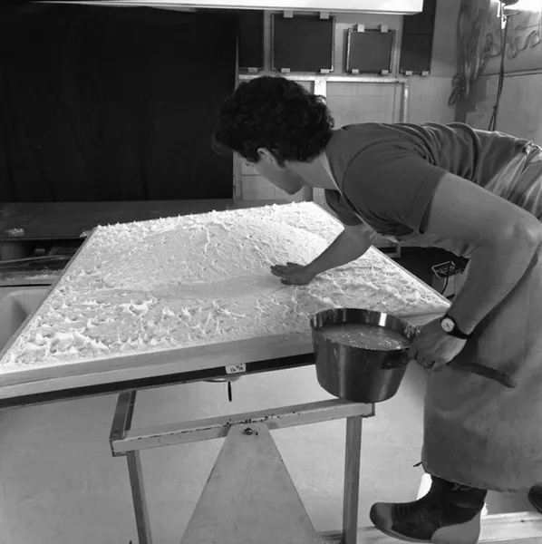 Black and white photo of man adding pulp along the perimeter of the dome-shaped section by hand