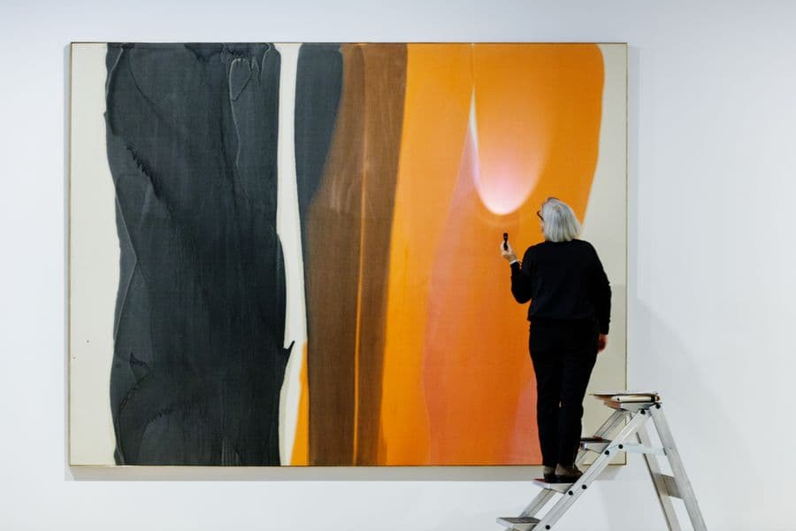 Photograph of red and black abstract painting being observed by conservator with flashlight on step stool