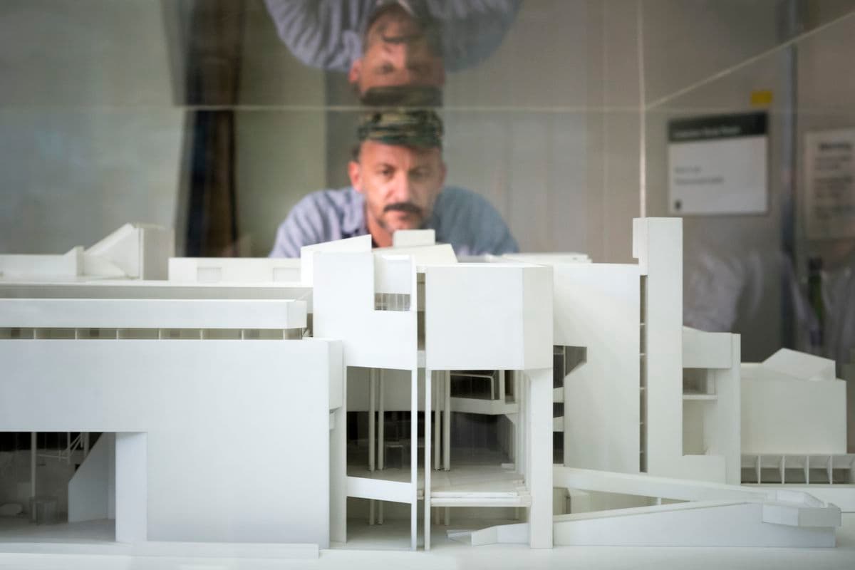 A white male looks into a perspex box which hold a white maquette of the National Gallery building