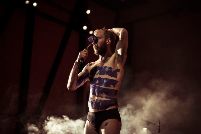 Semi naked bearded man painting purple paint on his body using a paint roller