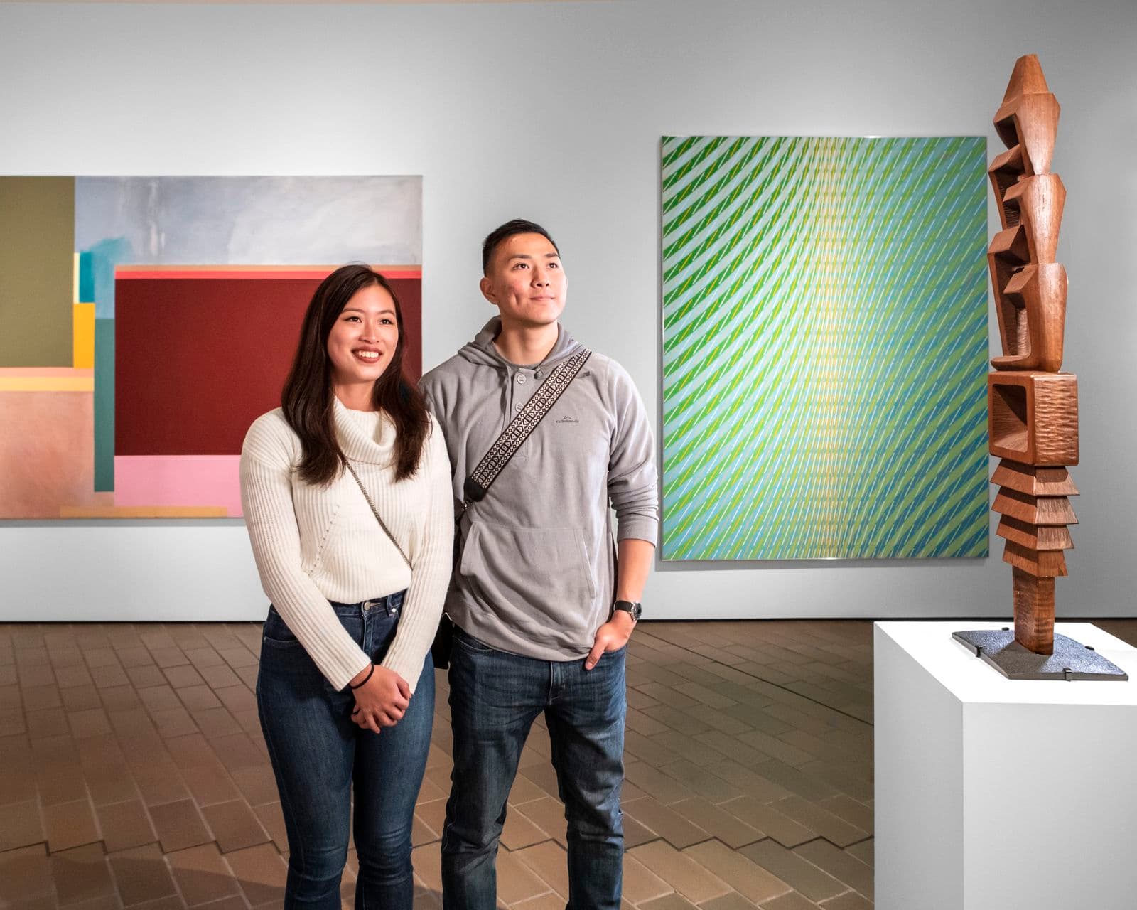 Photograph of couple standing in front of sculpture with paintings around them