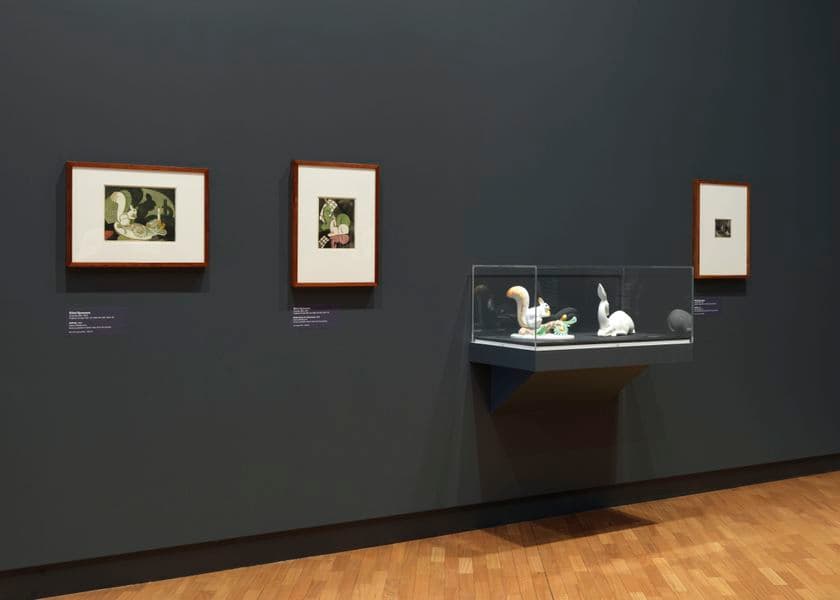 A grey wall with two works of art on the left, and a display cabinet on the right
