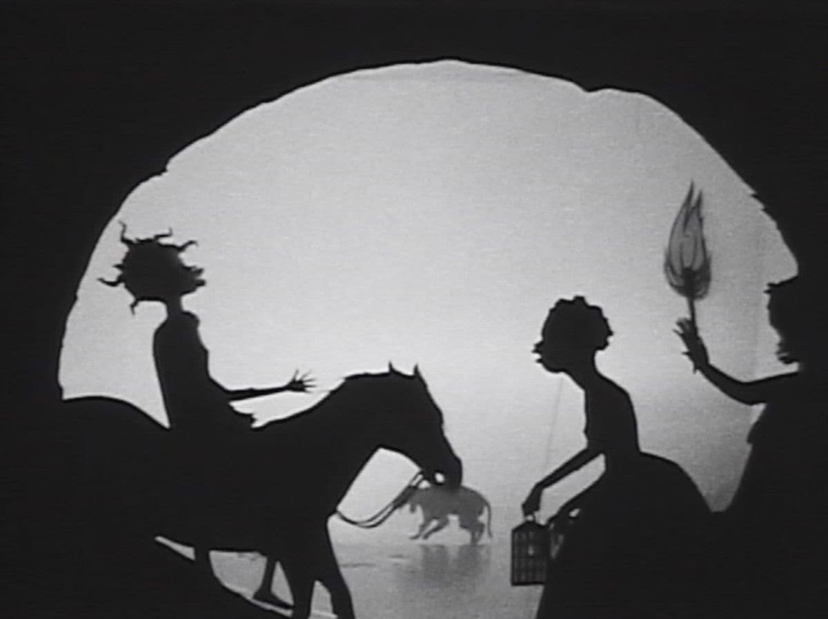 A black and white still of a silhouette film work showing a figure on a horse, a woman and a figure holding a flaming torch