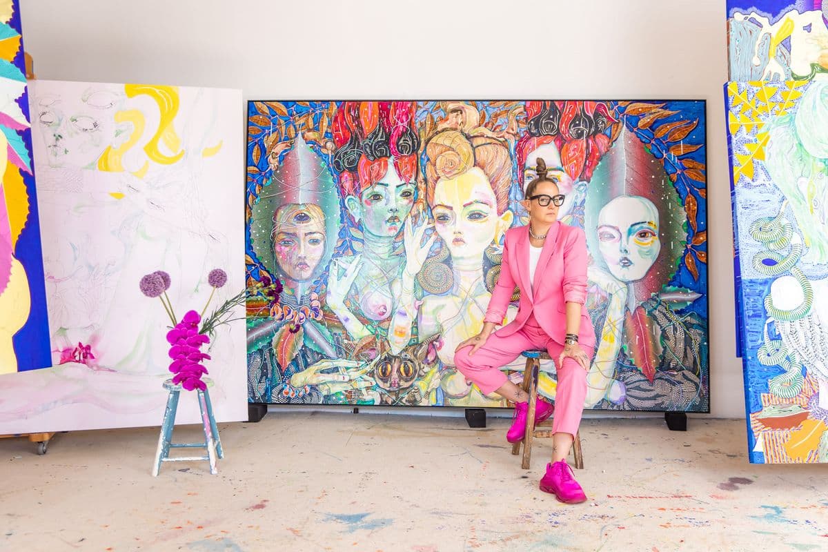 Artist Del Katheryn Barton sitting on a stool in front of a large painting