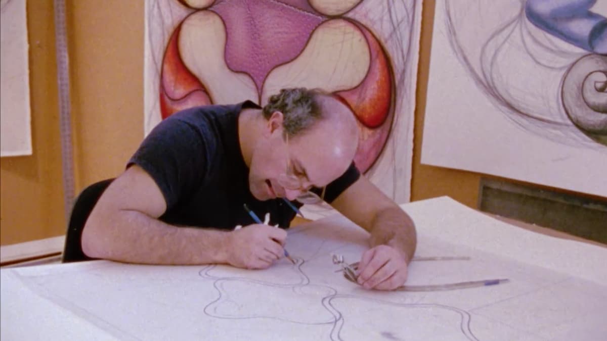 A video still of a man drawing in a studio