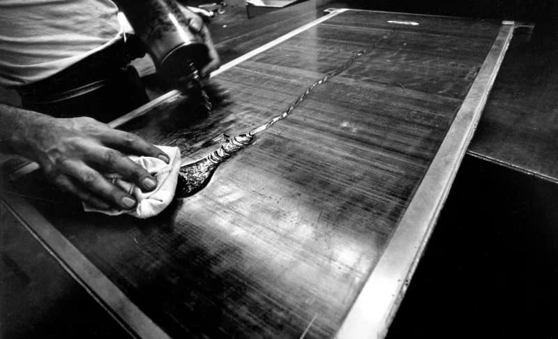 Black and white photo of The embossing plate for ‘Light bulb; from Lead relief series’ is cleaned by an unidentified staff member