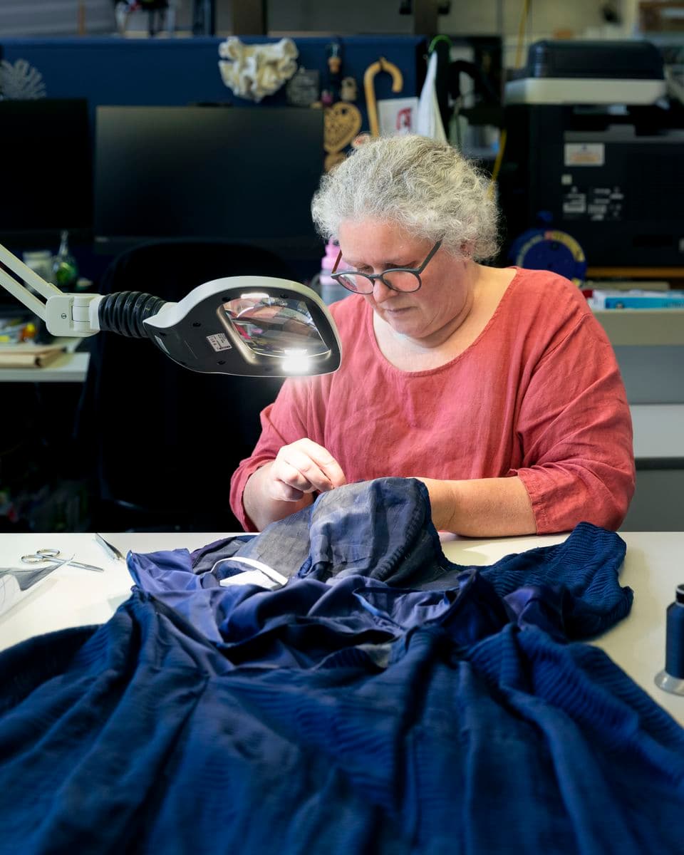 Colour photograph of Textiles COnservator Micheline Ford repairing a blue Givenchy cocktail dress