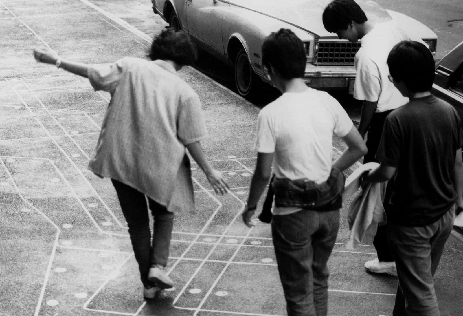 A black and white photo of kids playing in a public artwork which appears as chalk on the sidewalk