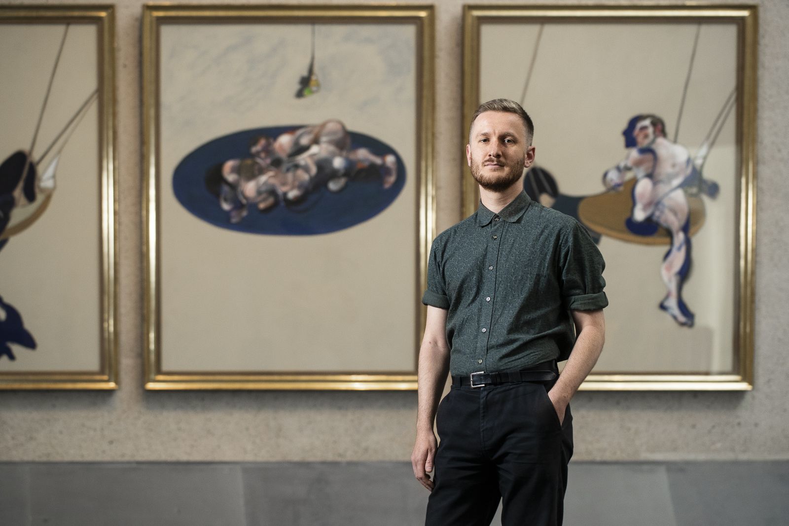 A man stands in front of three paintings.