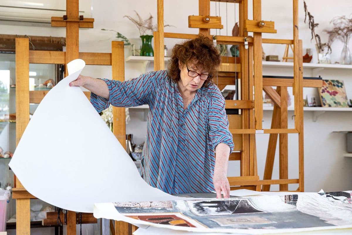 A photo of a woman artist working with a print work in a studio with easels in the background