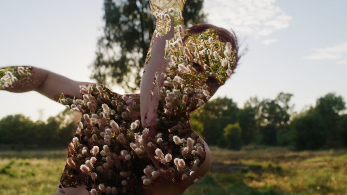 Video still of man standing close to camera with floral imagery projected onto naked body