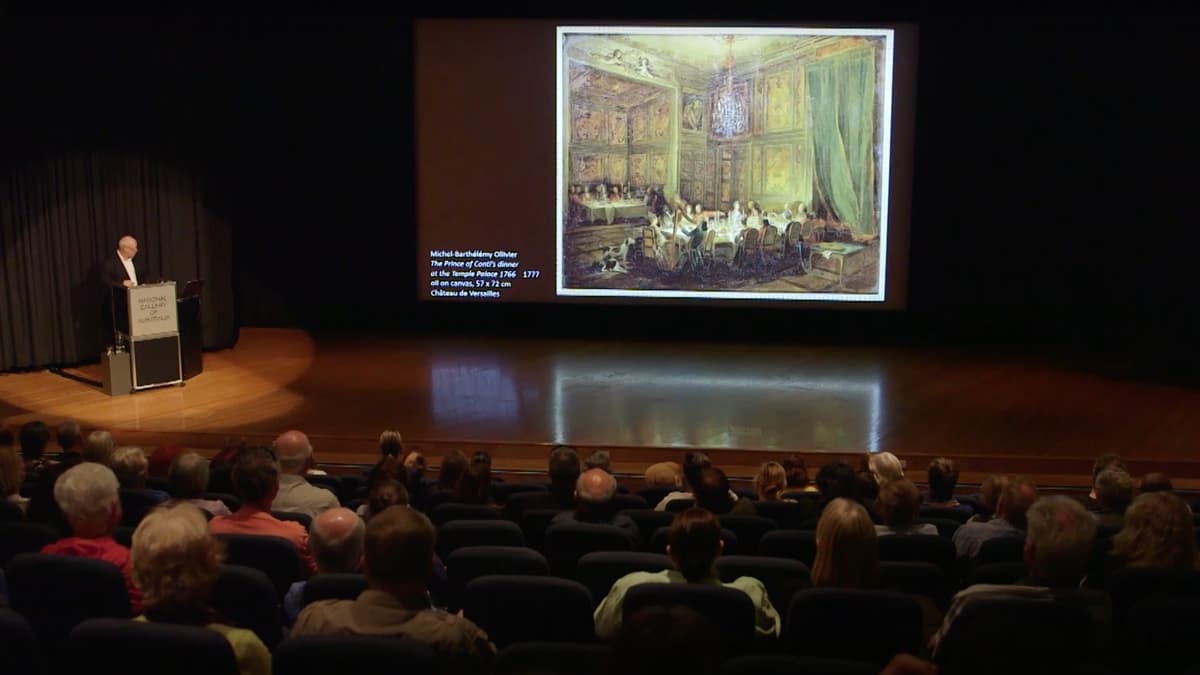 A video still of a man giving a lecture to a seated audience