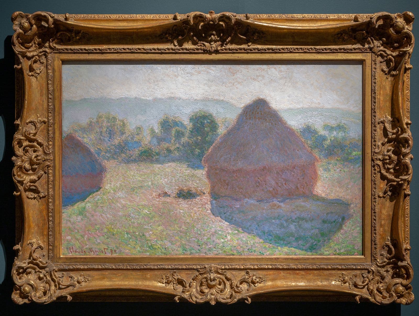 A gold frame holds a painting of haystacks