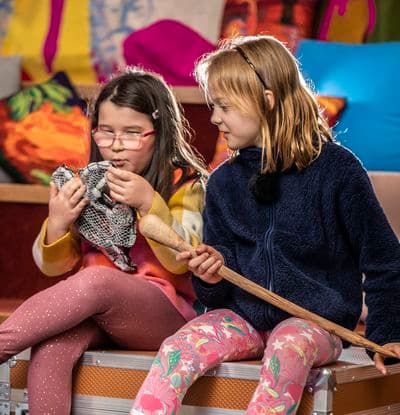 Two young girls are sitting on top of a large orange case, holding and examining objects