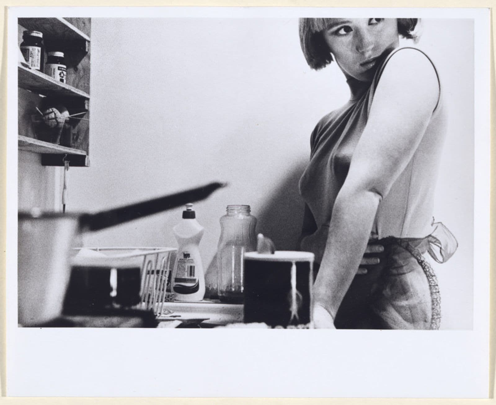 Black and white photograph of a woman standing by a kitchen sink