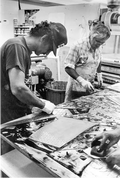 Black and white photo of Frank Stella and Kenneth Tyler inking relief sections of a ‘Swan engraving’ plate and wiping the plate with scraps of newsprint