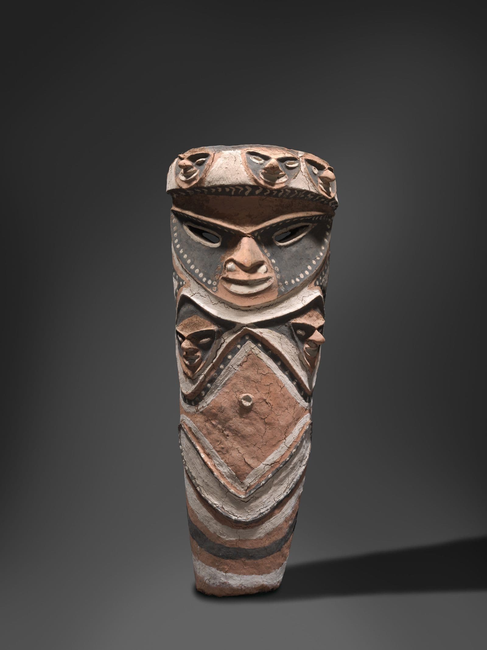 Traditional Vanuatuan sculpture depicting a central face accompanied by five other faces above and below. Painted in white, black and ochre
