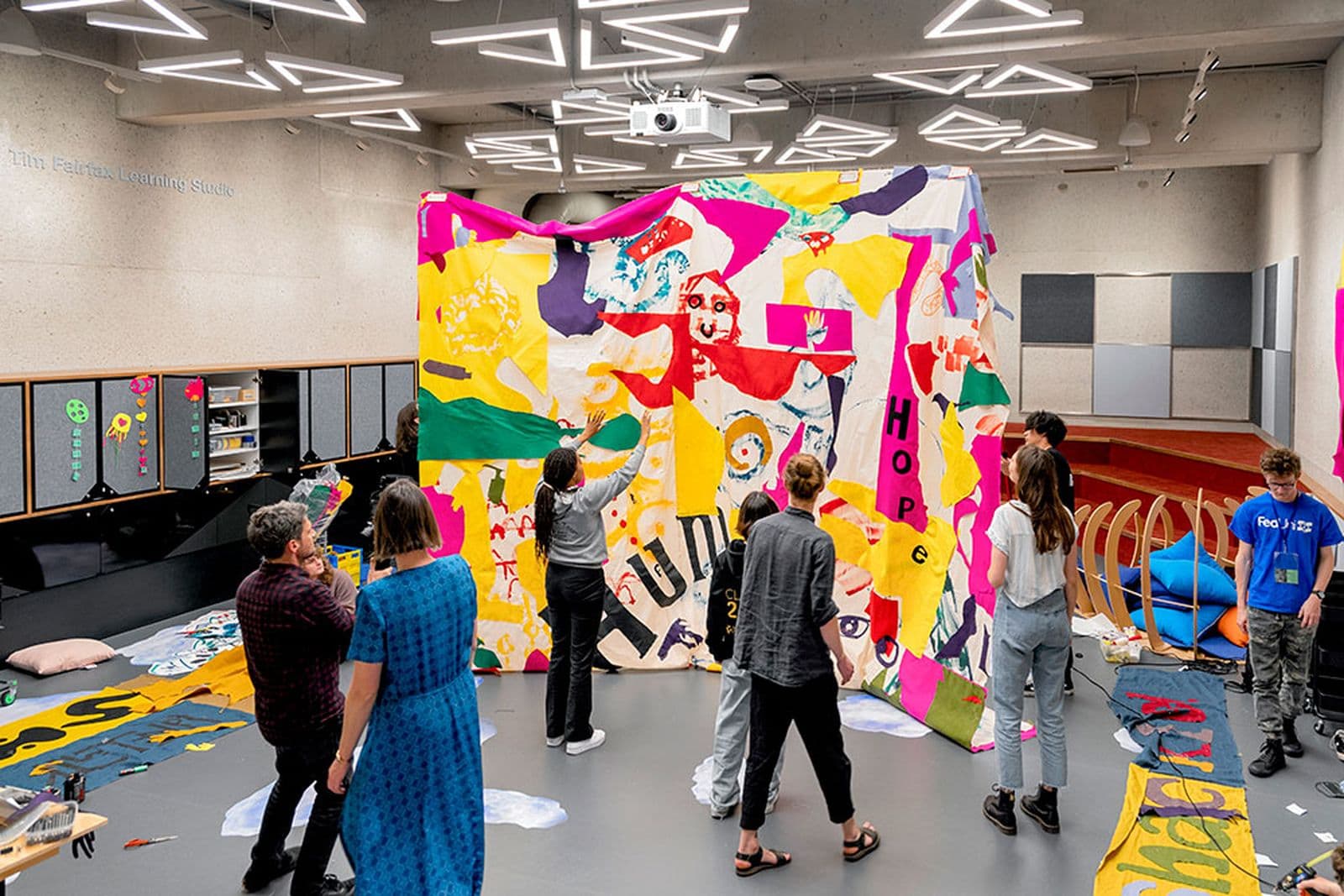 A group of people stand in front of a colourful patchwork fabric