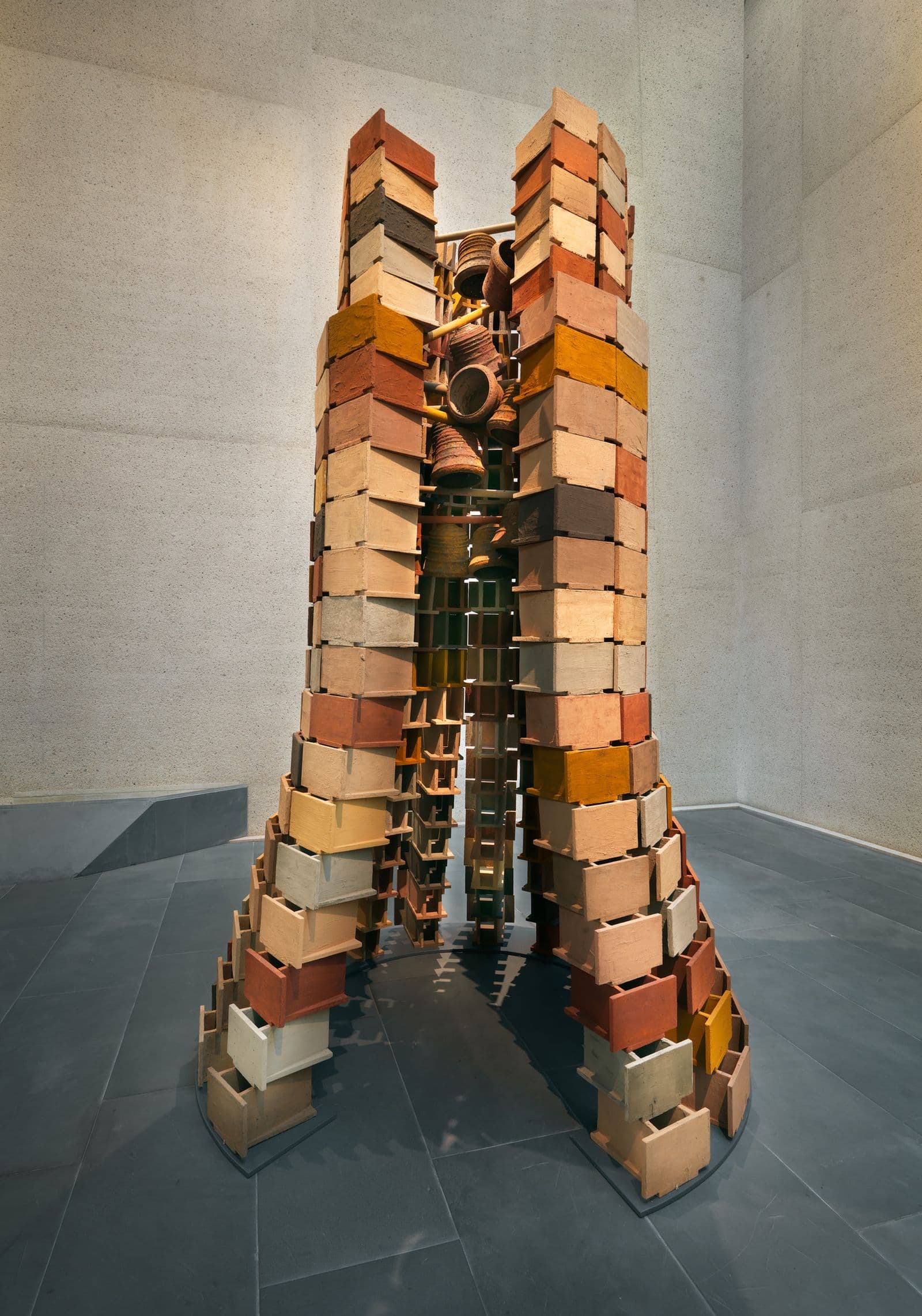 Large sculptural work of stacked wood, brass bells, and medicinal herbs