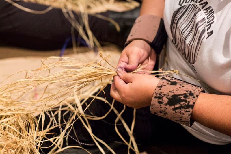 close-up photo of a pair of hands holding and weaving with native grasses