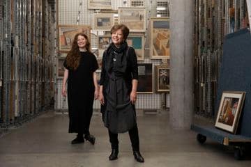 Two women are standing in a painting storage room