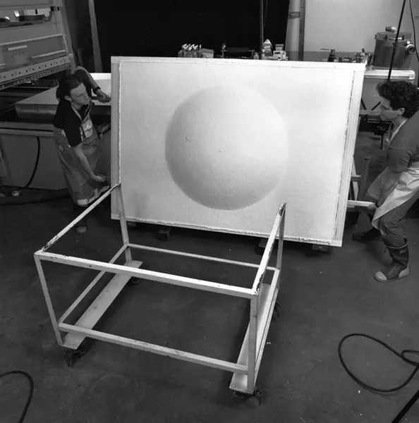 Black and white image of newly made paper pulp dome sheet being lifted by two men