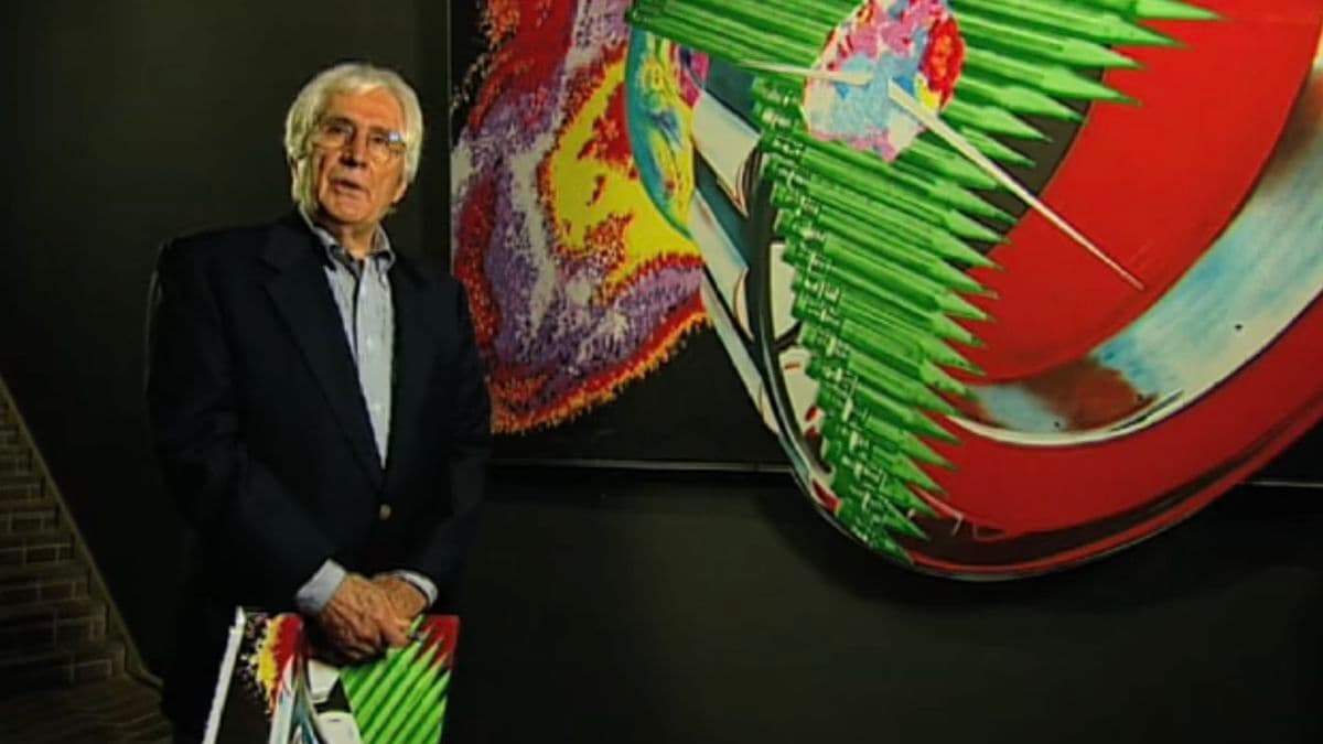 Video still of man standing next to painting.