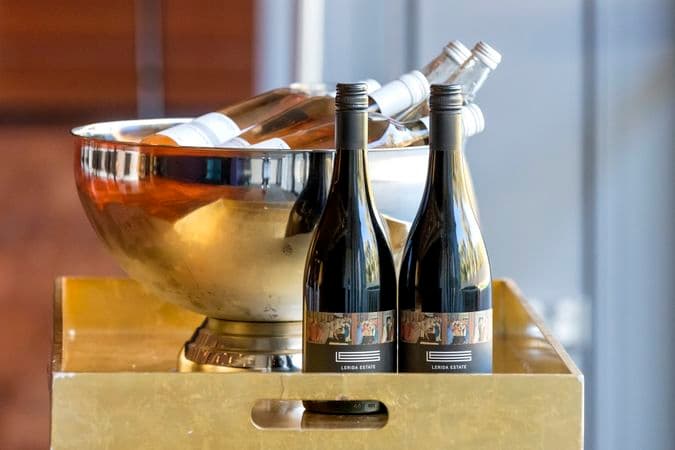 Two bottles of red wine stand on a tray in front of a cooler bowl filled with bottles of rose