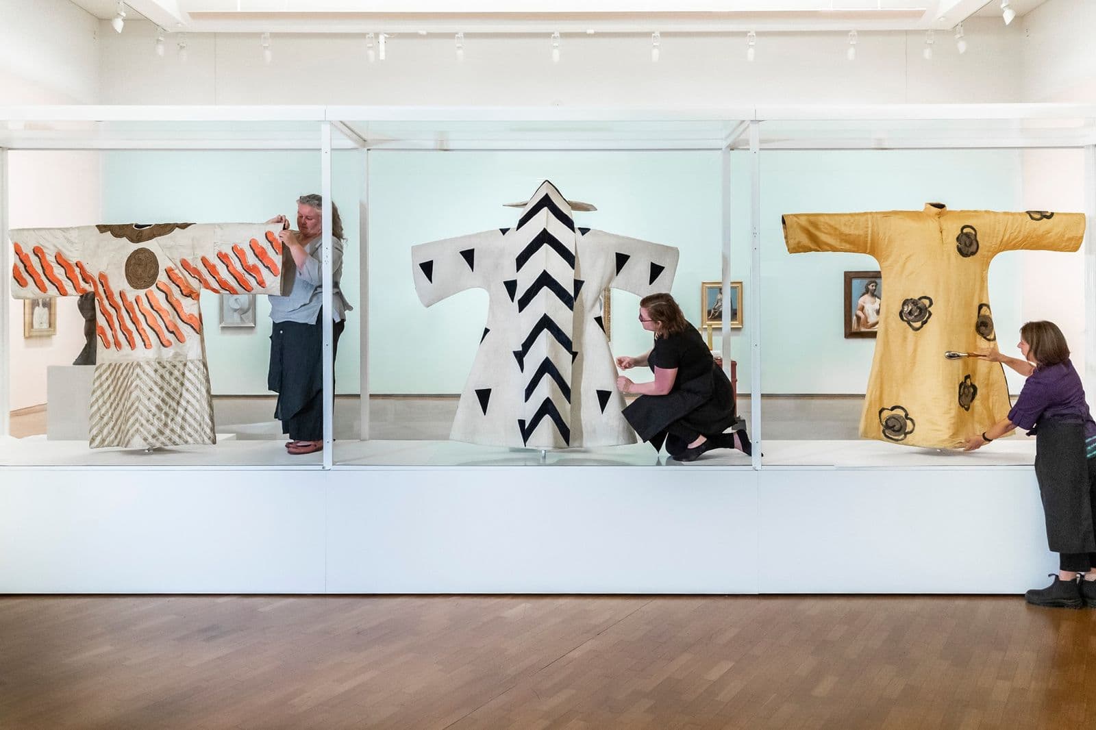 Photograph of textile conservator working on three hanging robes on display