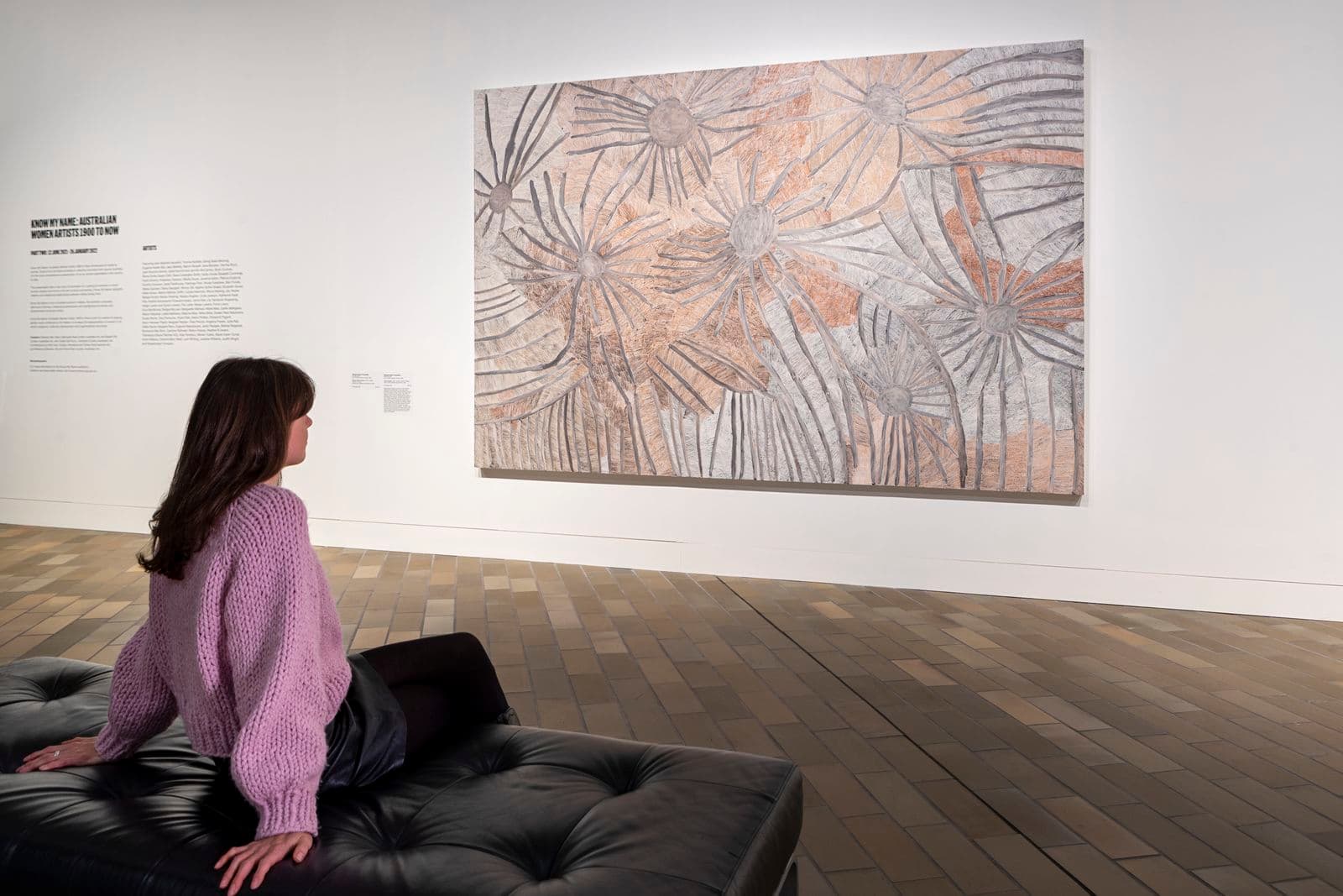 Photograph of woman sitting on black seat looking at artwork