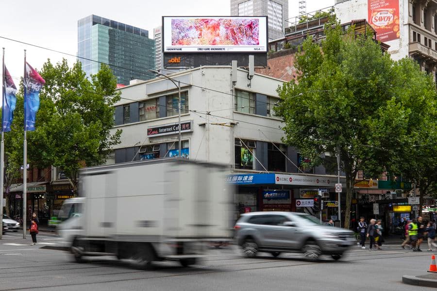 Image of indigenous artwork on billboard on top of building on a busy city street