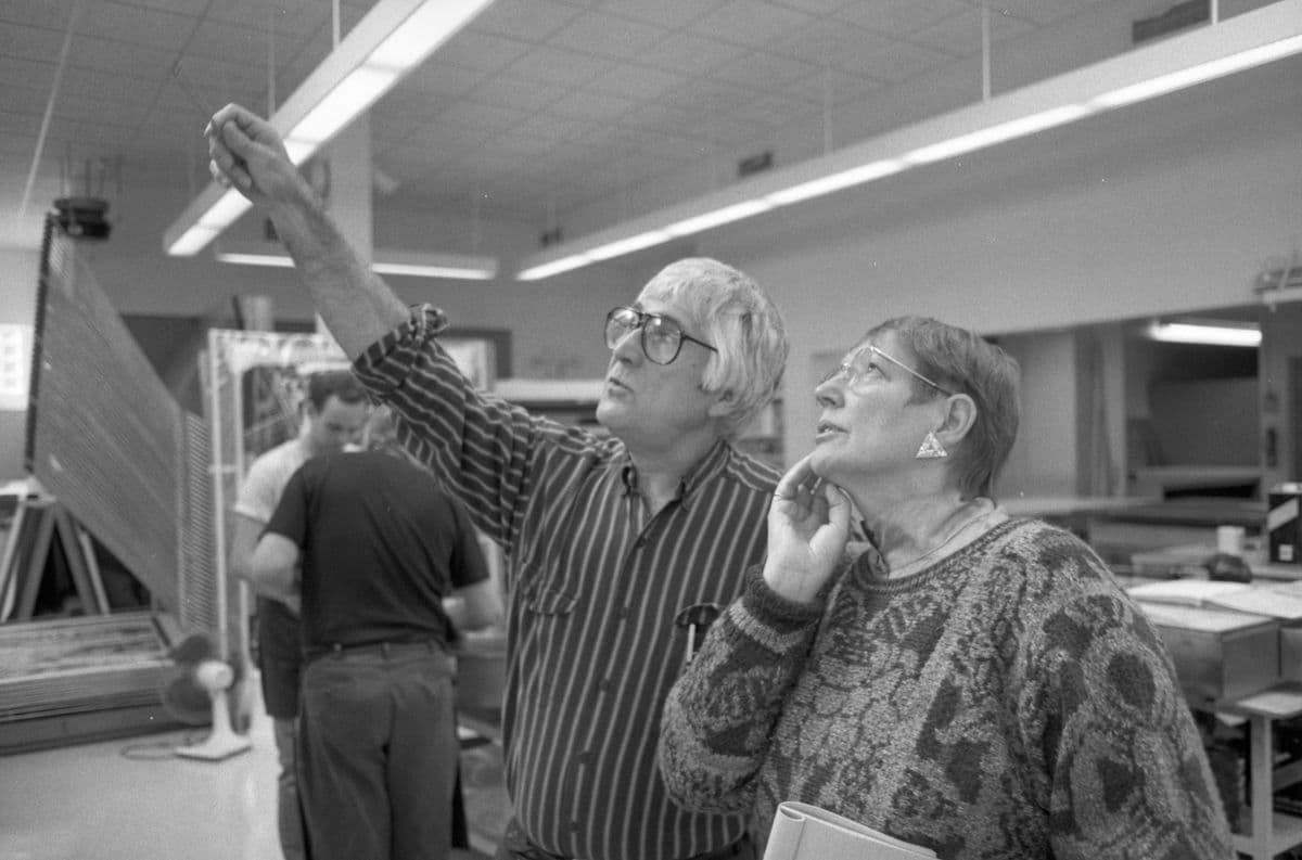A man and a women look towards an artwork that is out of shot. The man it pointing with a pencil and they are both looking in that direction.