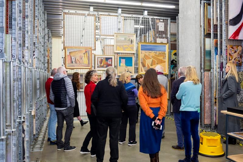 Photograph of visitors in the art storage room with paintings hanging