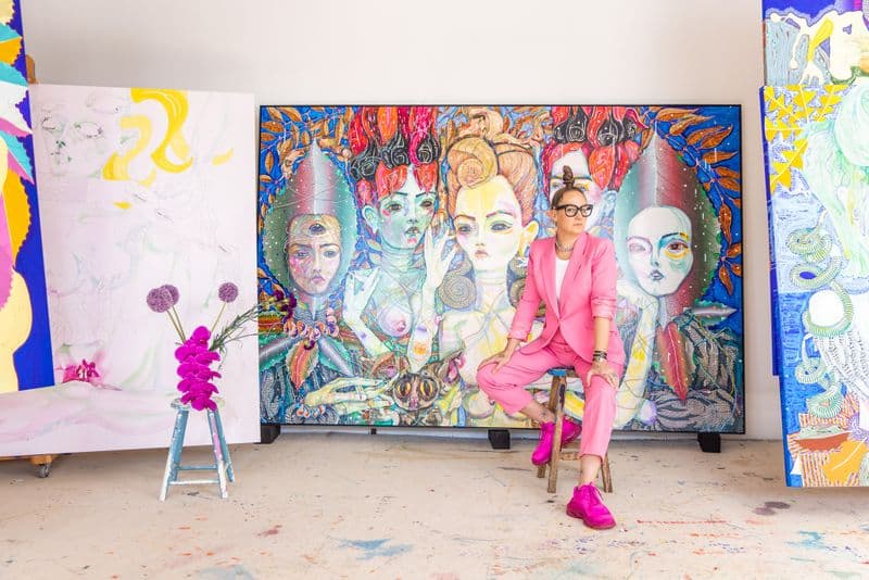 Artist Del Katheryn Barton sitting on a stool in front of a large painting