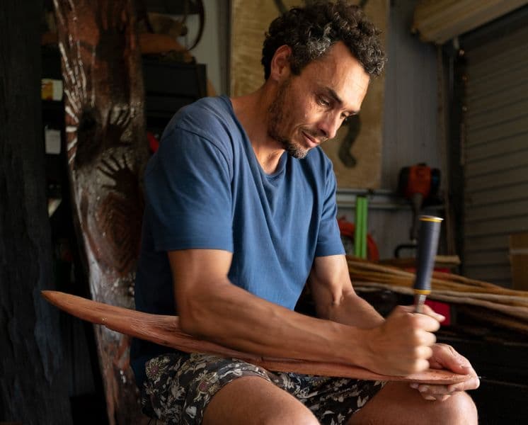 Photograph of artist in workshop on stool carving wood