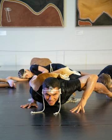 A young male dancer hovering on the floor with other dancers lying on the ground behind him
