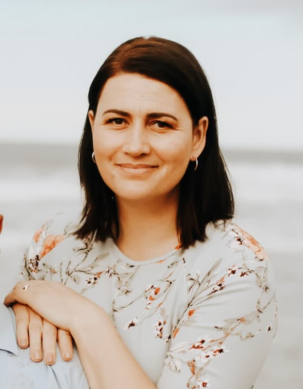 Portrait photo of female wearing a floral blouse, with a dark brown shoulder length straight hair with her hands resting on another person's shoulders