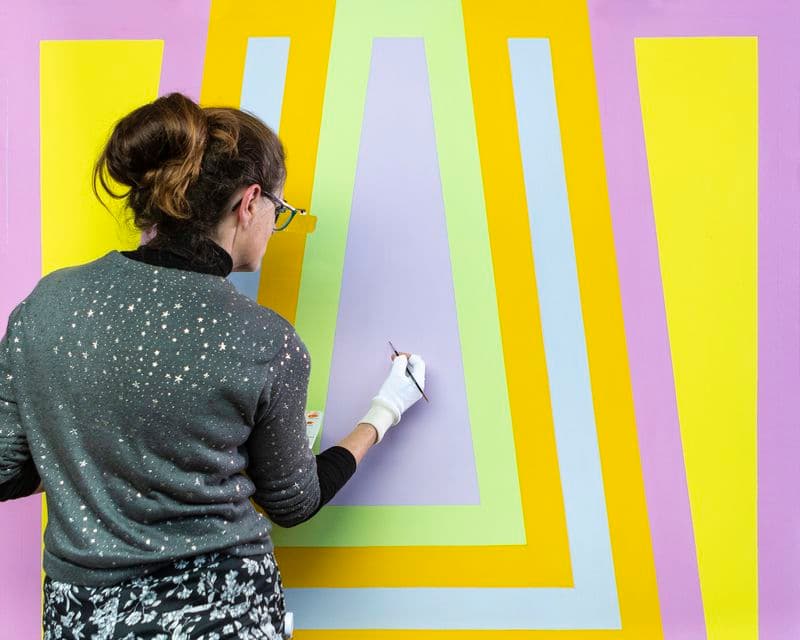 Photograph of conservator restoring colourful painting with paint brush