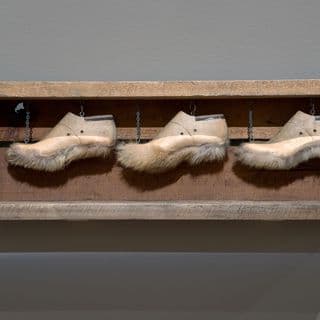 A sculpture of three shoe lasts with fur attached to the soles, fastened in a row alongside each other inside a timber rectangle frame