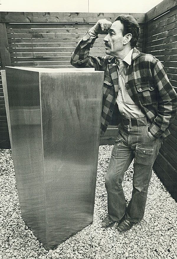 Black and white photograph of Kosso Eloul leaning on a sculpture