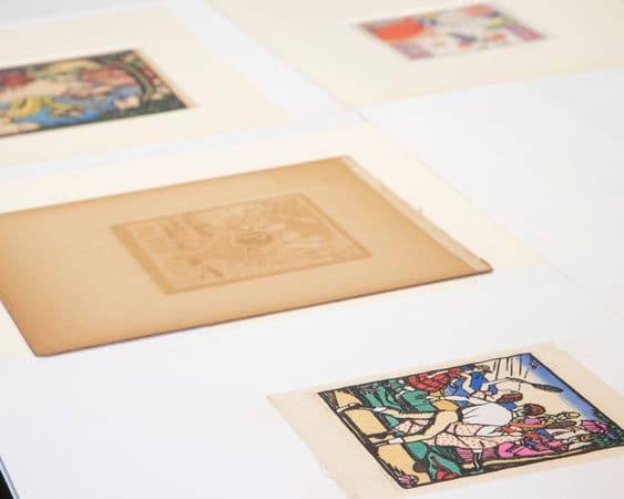 a number of small works of art on paper are laid out on a table for conservation treatment