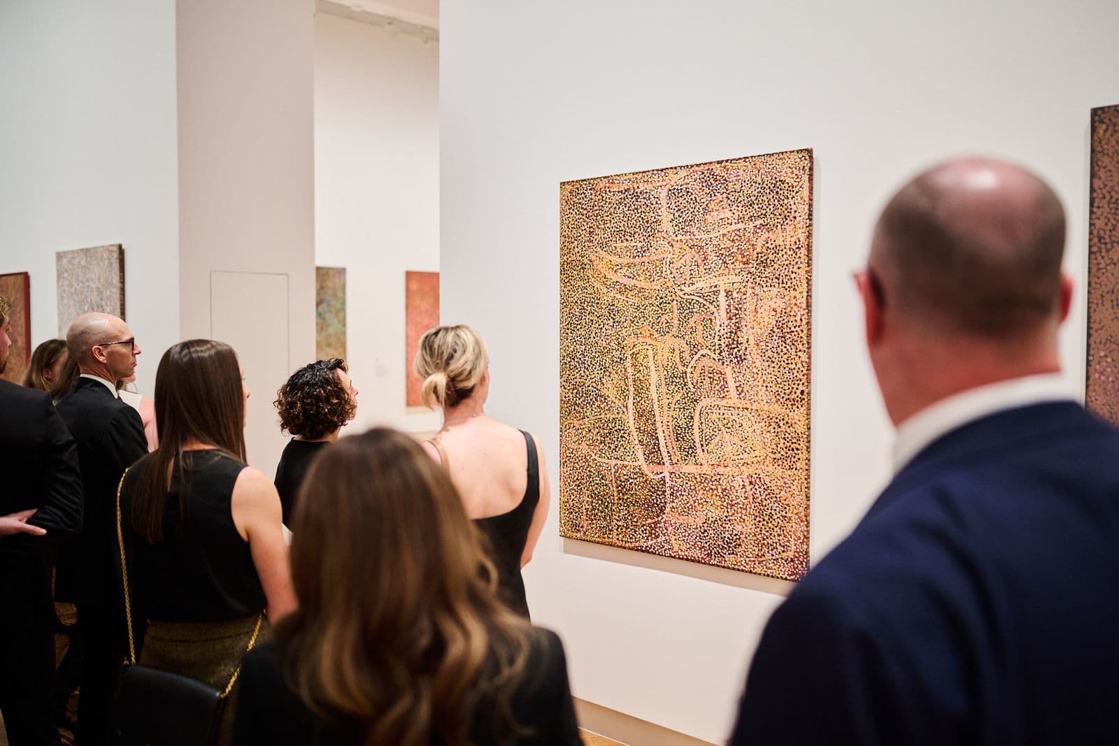 Photo of a group of people looking at an indigenous artwork in a gallery space