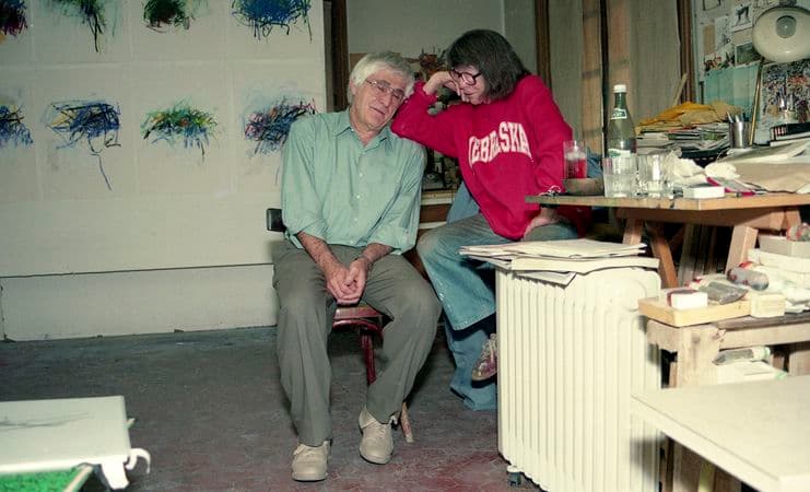A photograph of Joan Mitchell and Kenneth Tyler sitting on chairs in an artist studio.