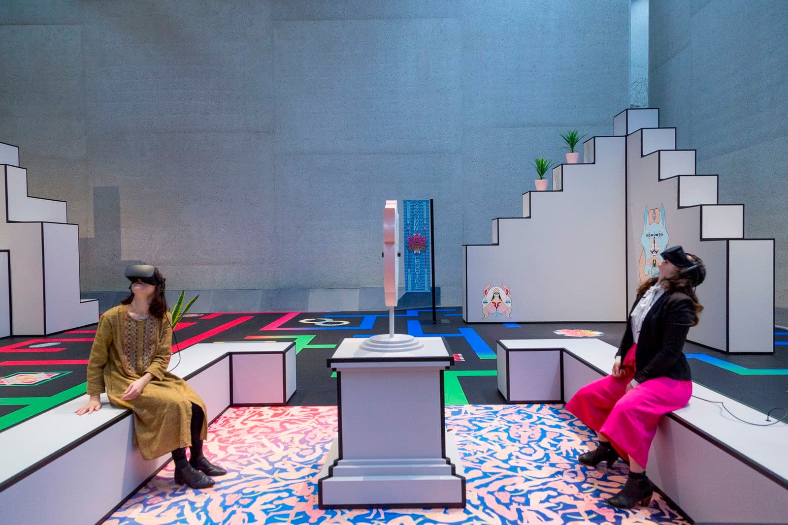 Two people wearing virtual reality headsets sit opposite each other in an art installation