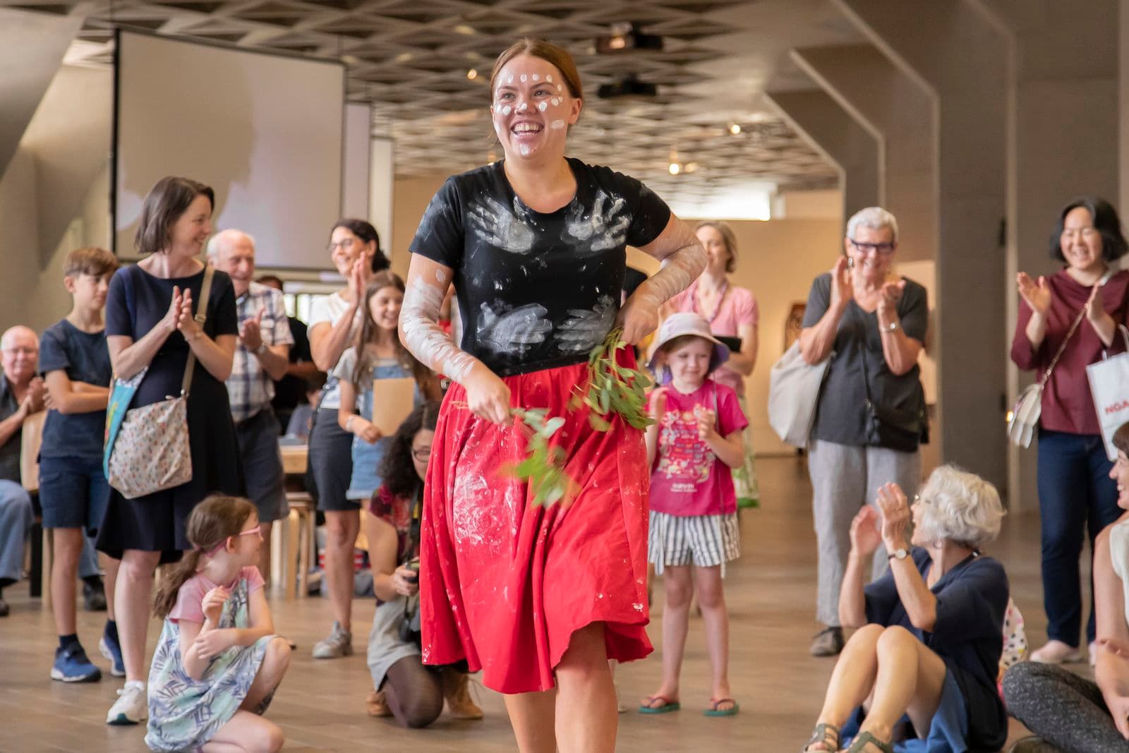 Photograph of woman performing Indigenous dance with visitors clapping in background