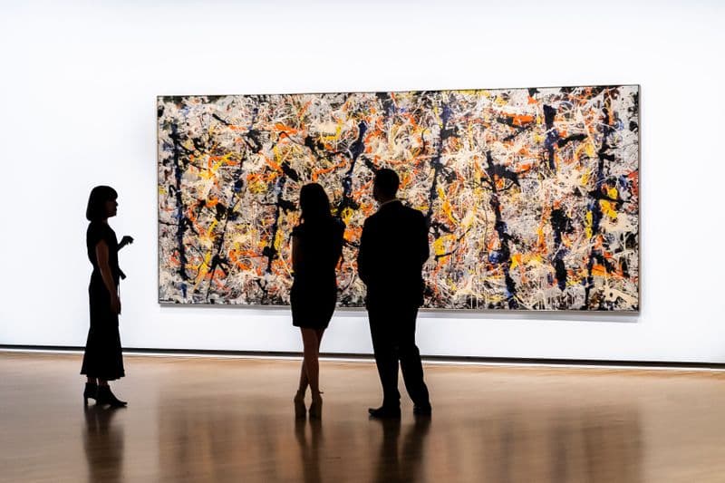 three people are standing in front of a large painting on canvas hanging on a wall