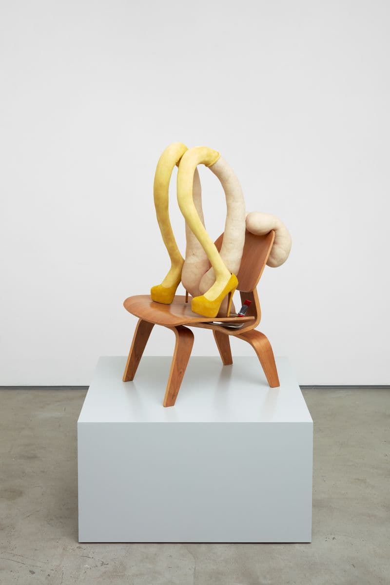 Sculpture of abstracted female legs and breasts on a wooden chairand yellow high heels